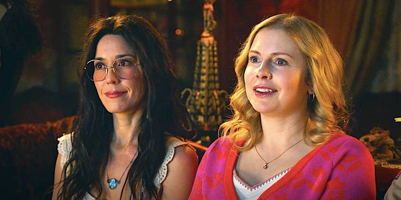 Rose McIver's Sam and Sheila Carrasco's Flower sit on a couch in Ghosts season 4 episode 10