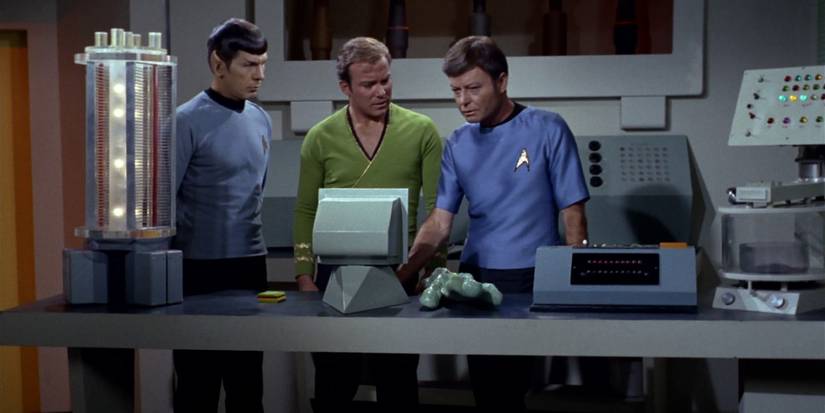 Kirk, Spock, and McCoy stand around a computer screen in Star Trek: The Original Series.