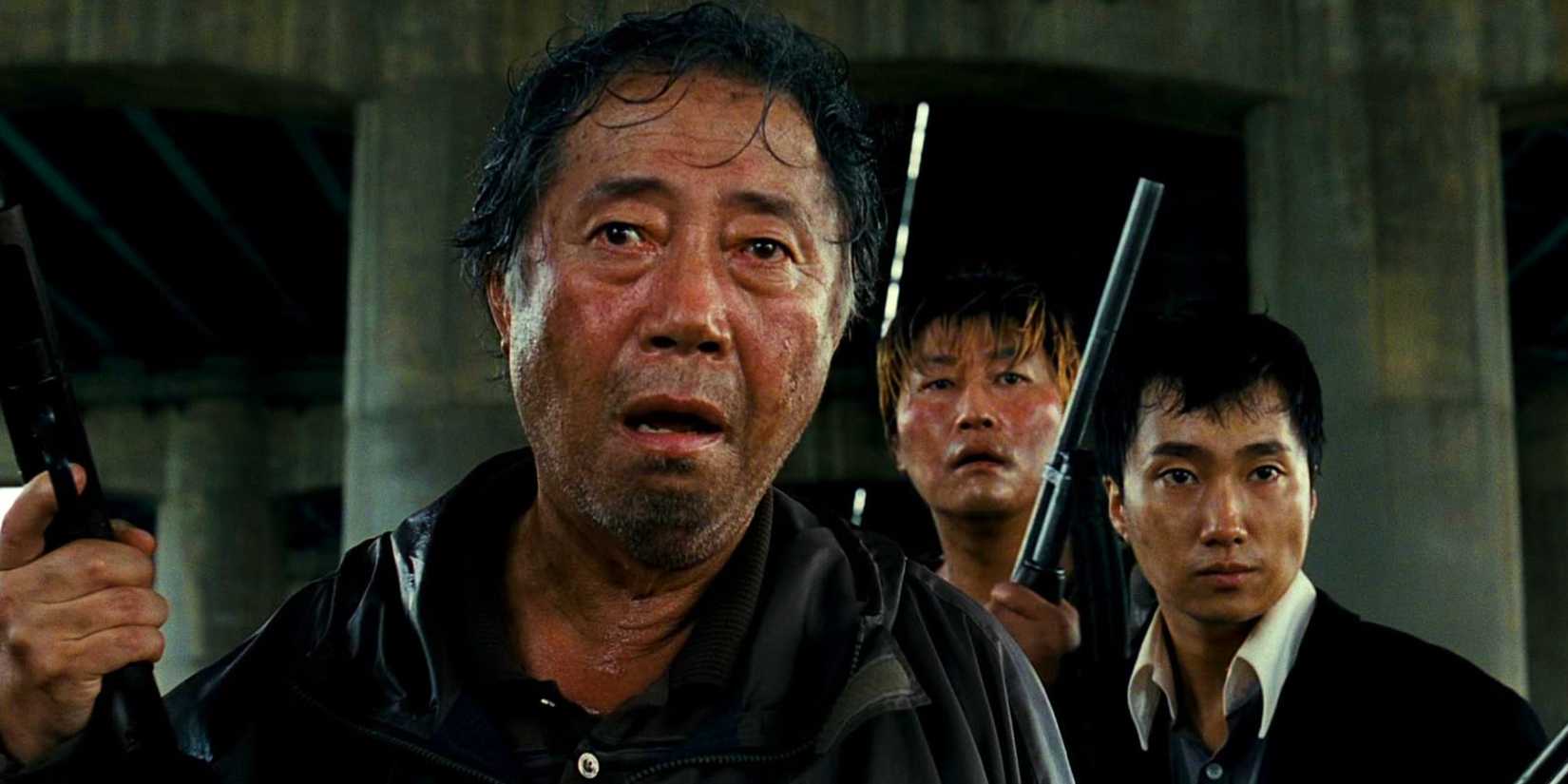 Image from The Host 2006 Bong Joon-ho showing a man looking shocked, standing in front of two other men with guns