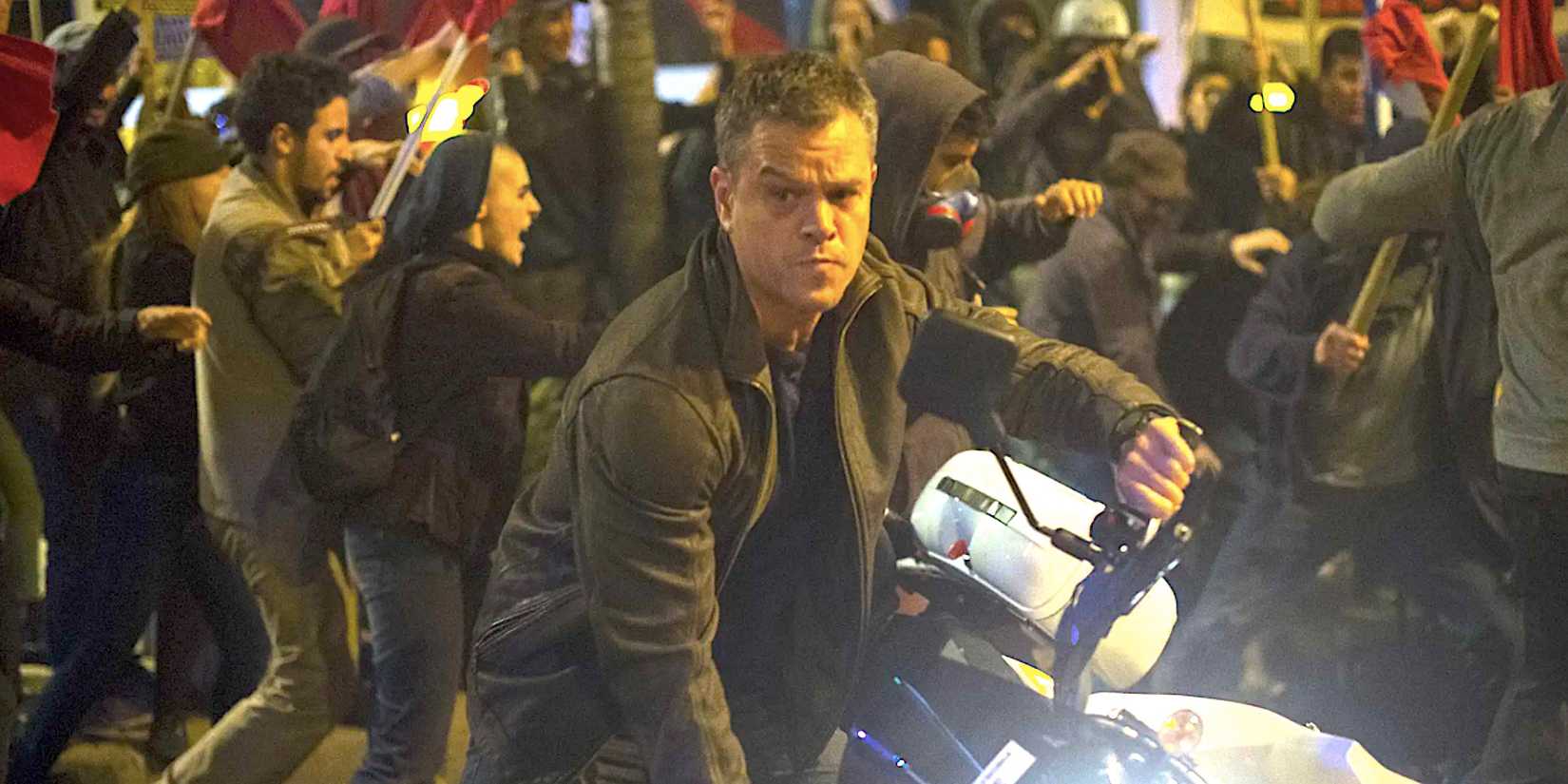 Matt Damon's Jason Bourne on a motorbike beside protestors on a busy street from Jason Bourne 2016