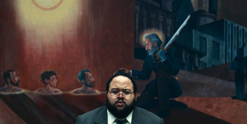 Dylan (Zach Cherry) with a mural of Kier behind him in Severance Season 2 Ep 9