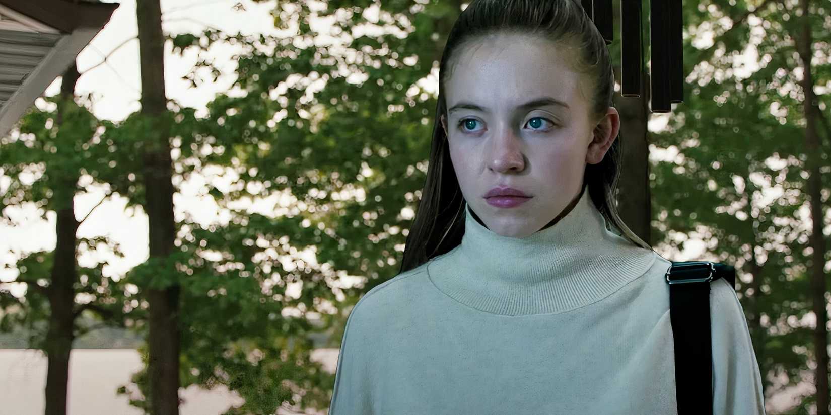 Sydney Sweeney standing and looking at something intently with trees in the background