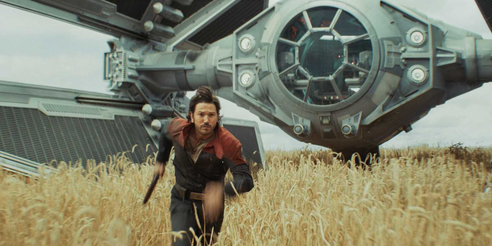 Cassian Andor (Diego Luna) running through a wheat field with a TIE Fighter in the background in Andor Season 2 Episode 3