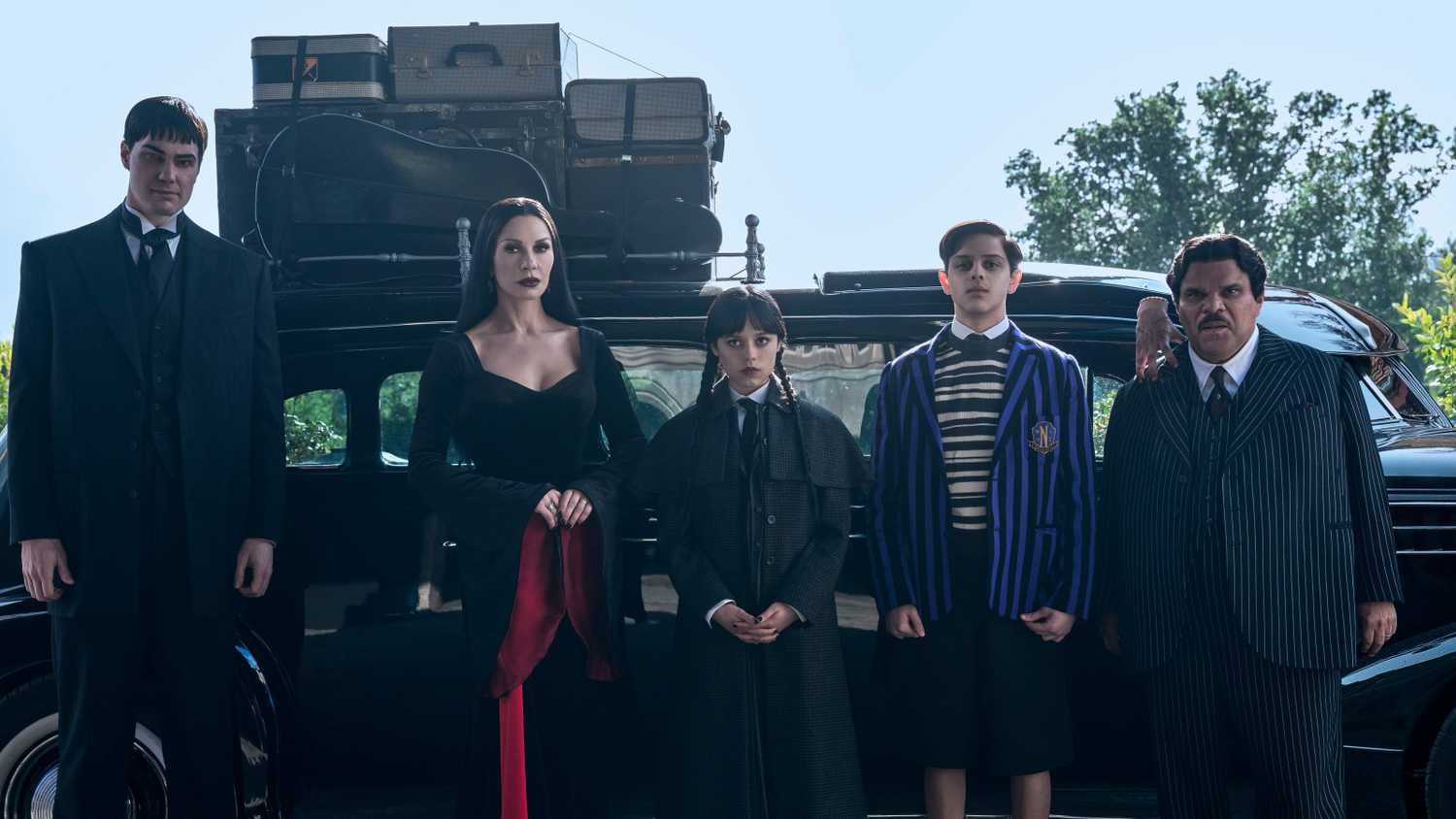 Lurch, Morticia, Wednesday, Pugsley, and Gomez Addams standing in front of their car in Wednesday season 2