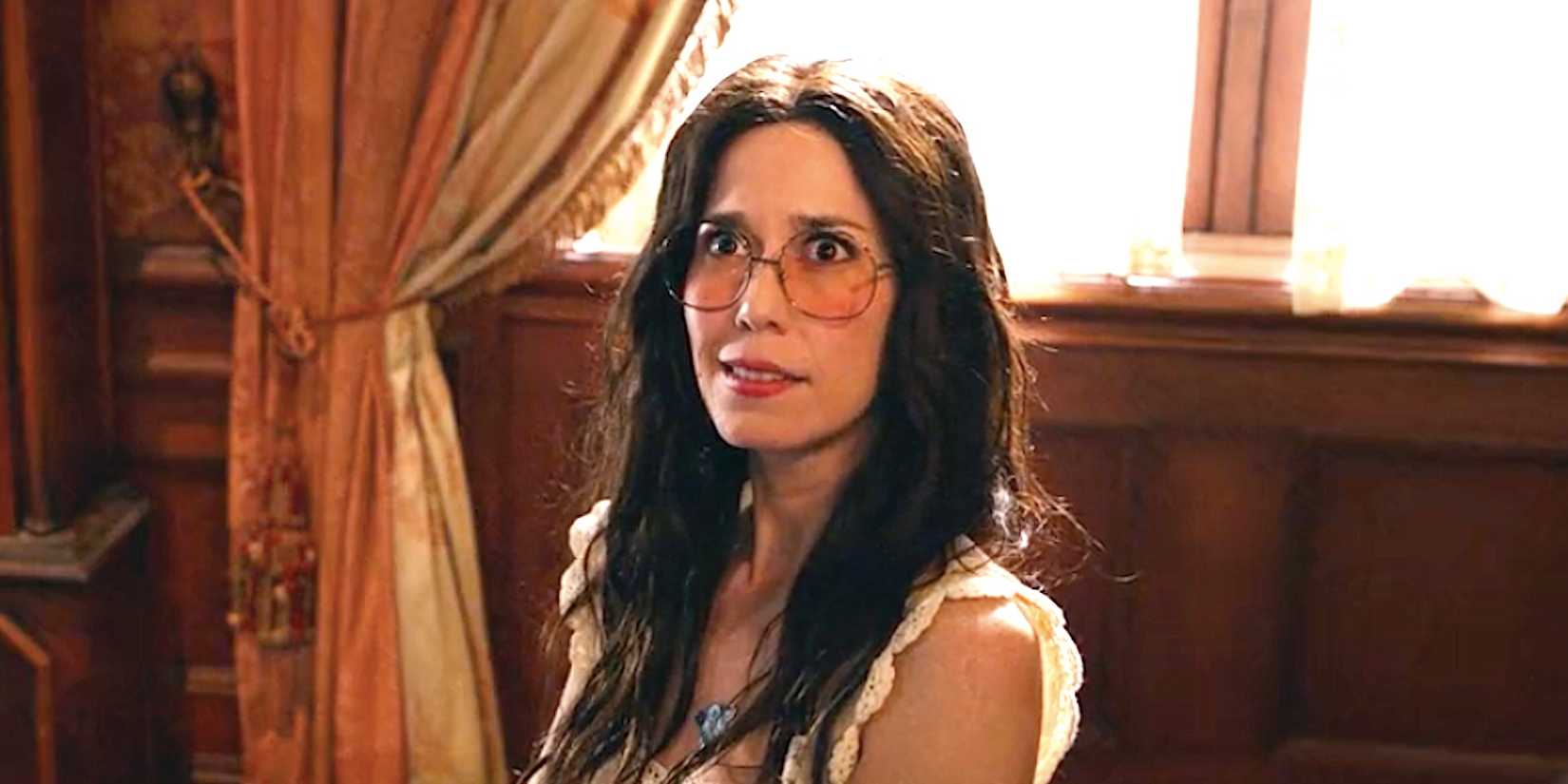 Sheila Carrasco como Flower sentada em uma cadeira com ar de dúvida em Ghosts temporada 4 episódio 18