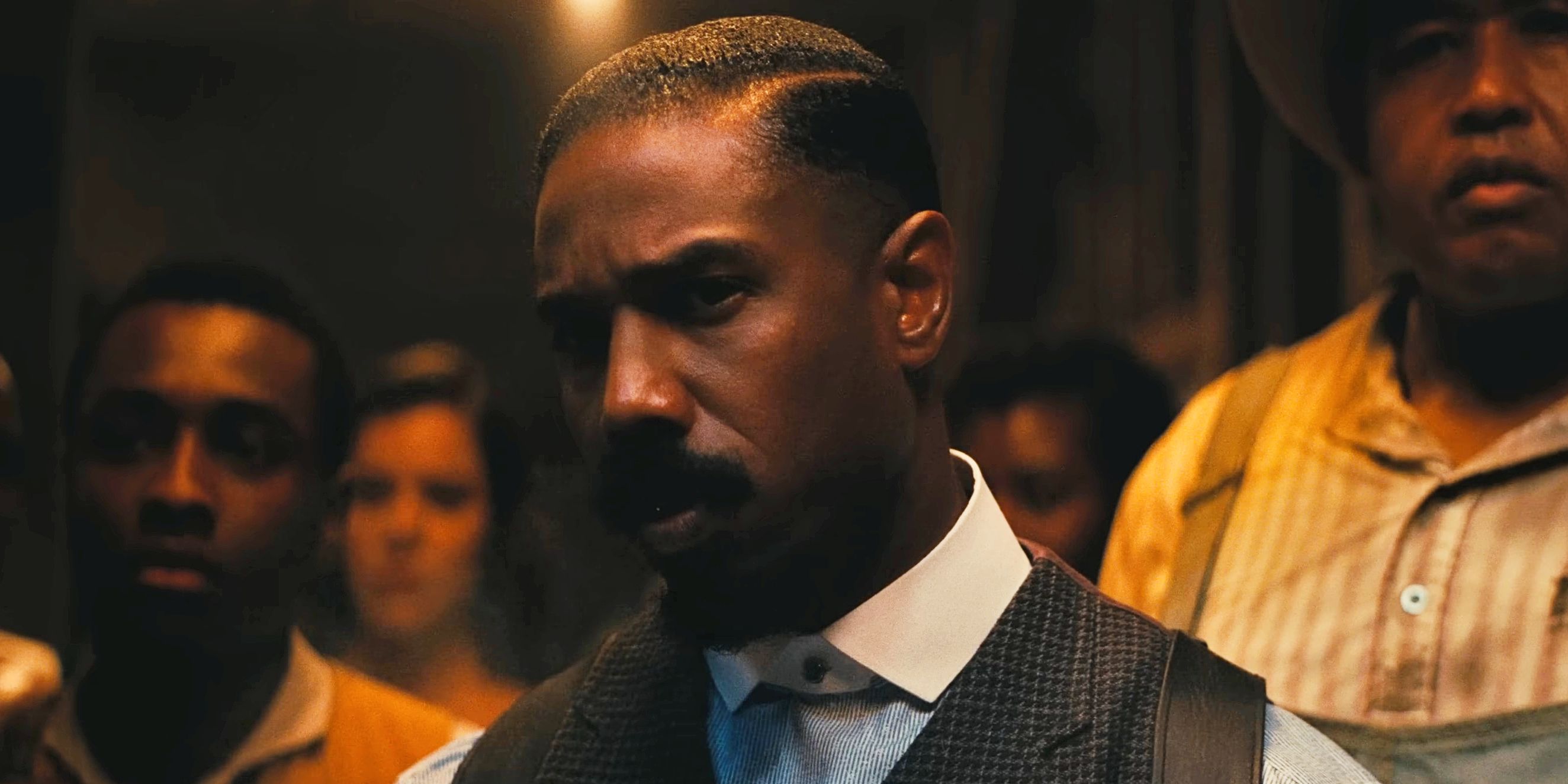 Smoke looking quizzically past the camera as people behind him look the same way in Sinners