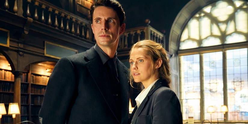 Teresa Palmer and Matthew Goode standing next to each other in the library in A Discovery of Witches