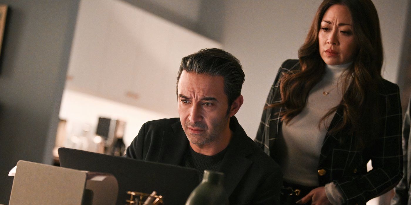 Reenie looks over Leo's shoulder, concerned, at a laptop