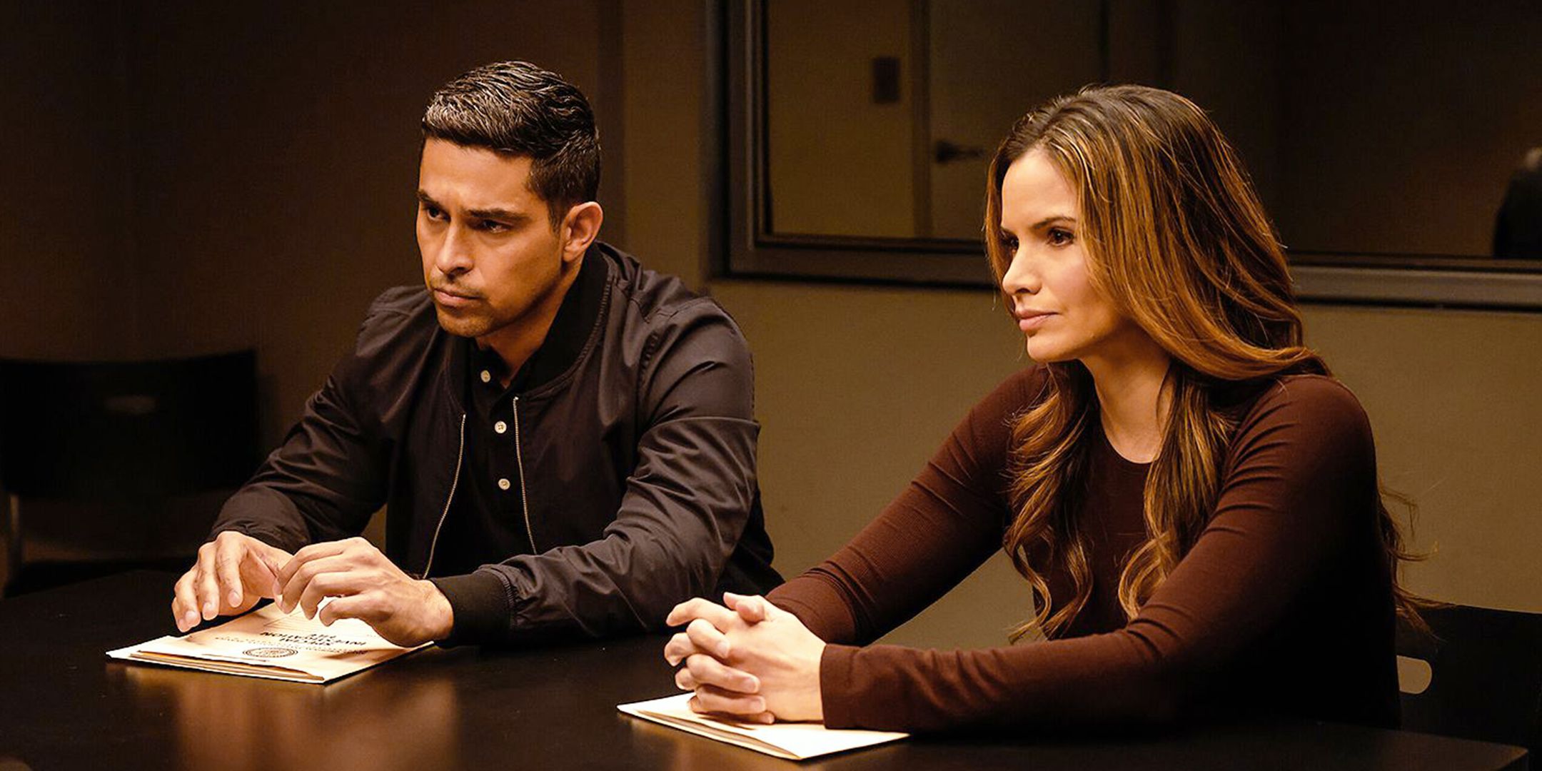 Wilmer Valderrama's Nick Torres and Katrina Law's Jessica Knight sitting at an interrogation table in NCIS