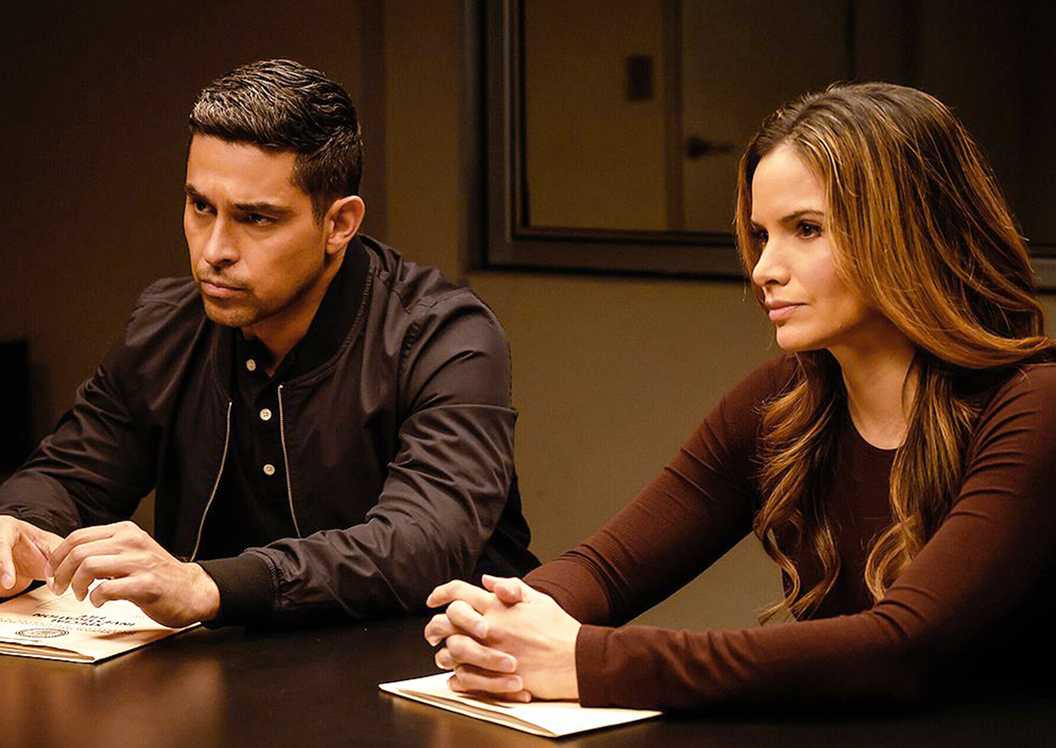 Wilmer Valderrama's Nick Torres and Katrina Law's Jessica Knight sitting at an interrogation table in NCIS