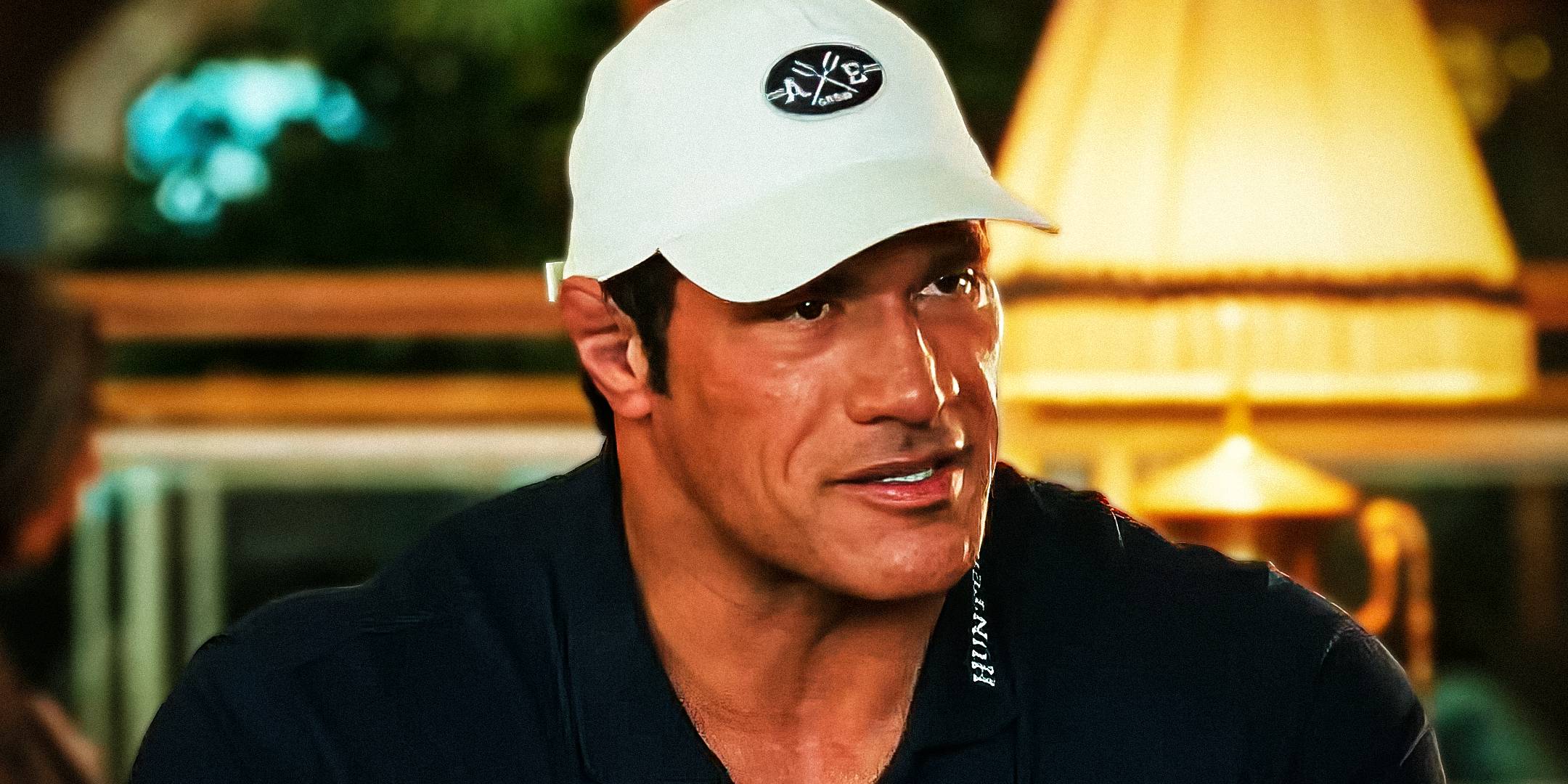 The Rock as Mark Kerr wearing a white hat and sitting down in The Smashing Machine