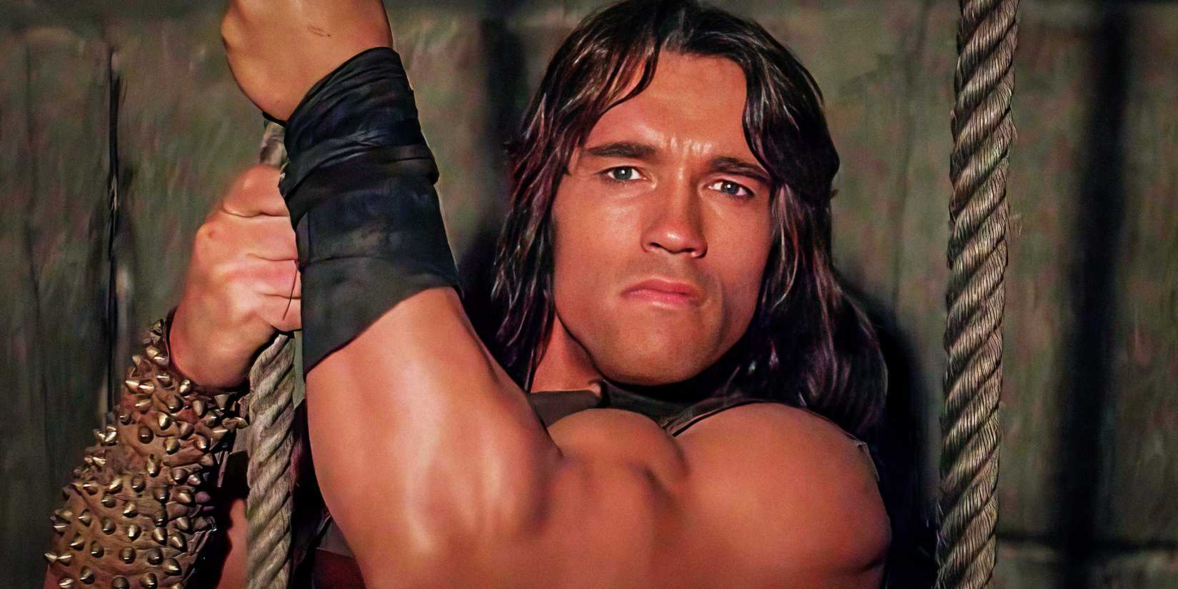 Arnold Schwarzenegger segurando uma corda como Conan em Conan, o Bárbaro