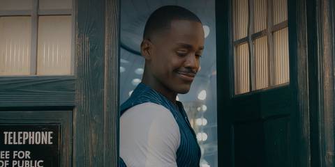 Ncuti Gatwa standing in the doorway of the TARDIS smiling downward