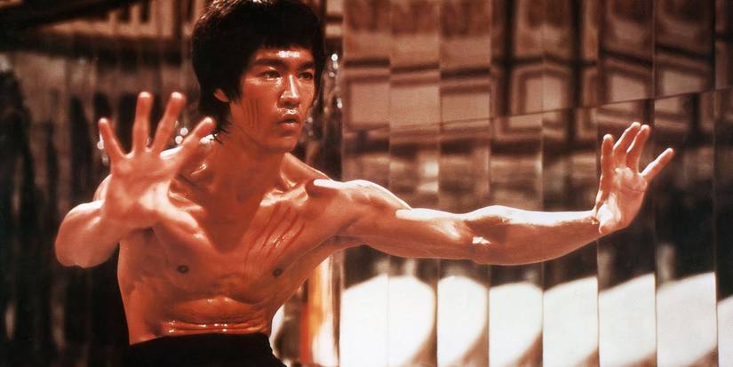 Bruce Lee stands with his arms outstretched in front of mirrors in Enter the Dragon