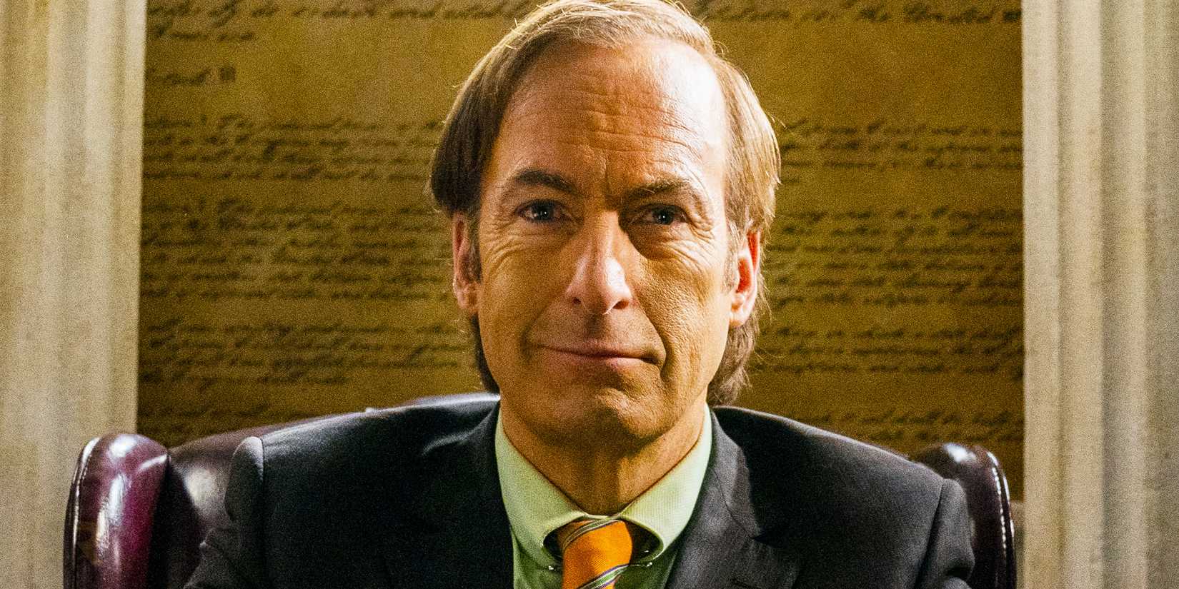 Jimmy McGill/Saul Goodman (Bob Odenkirk) sorrindo enquanto estava sentado em seu escritório em Better Call Saul Season 6