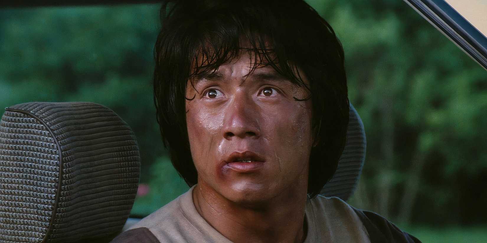 Jackie Chan looks up from the seat of a car he's sitting in.