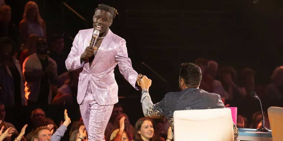 Jamal Roberts from American Idol wearing a shiny pearlescent suit fist bumping Luke Bryan while performing on stage.