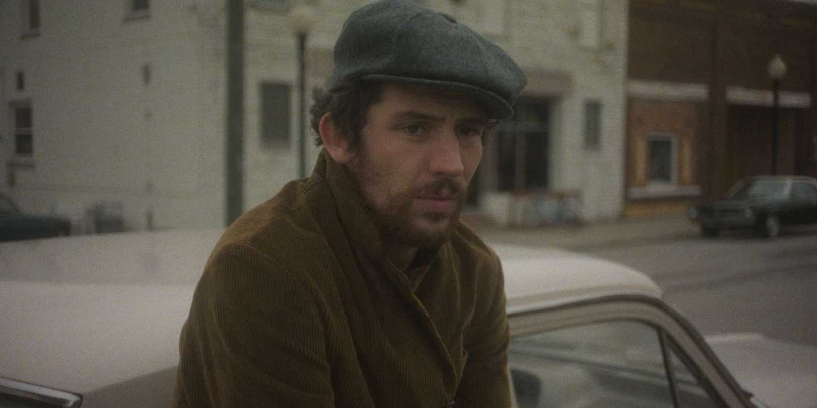 Josh O'Connor leans against a car with his arms crossed in The Mastermind