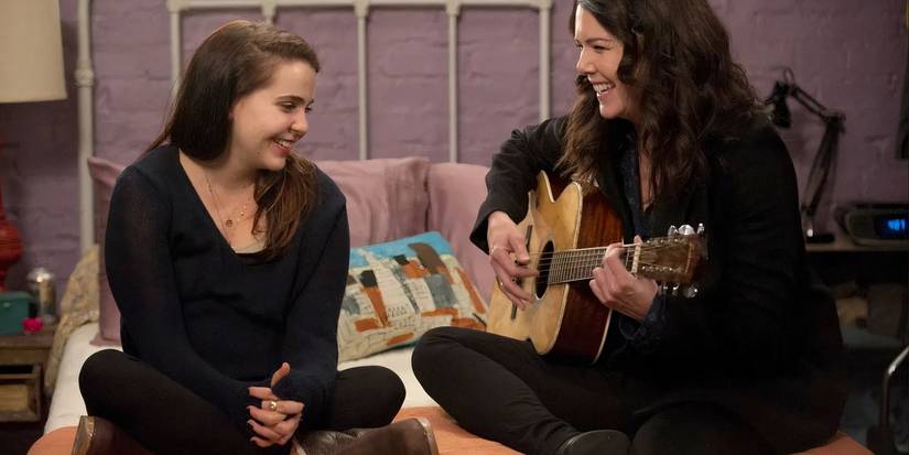 Lauren Graham as Sarah playing guitar on a bed next to a teenage girl in Parenthood