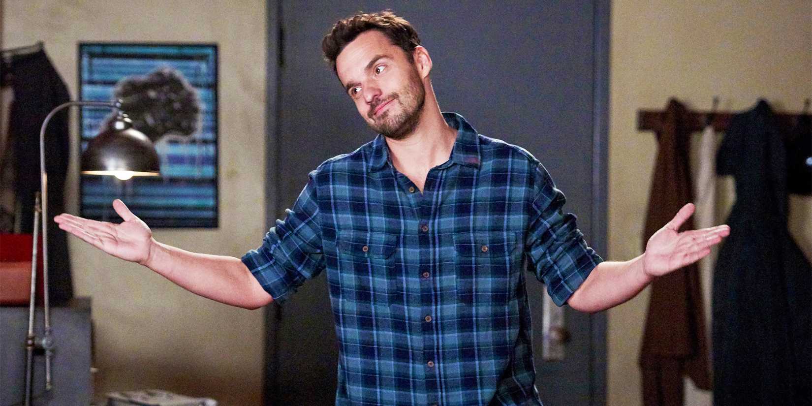 Jake Johnson como Nick Miller em New Girl, encolhendo os ombros e sorrindo.