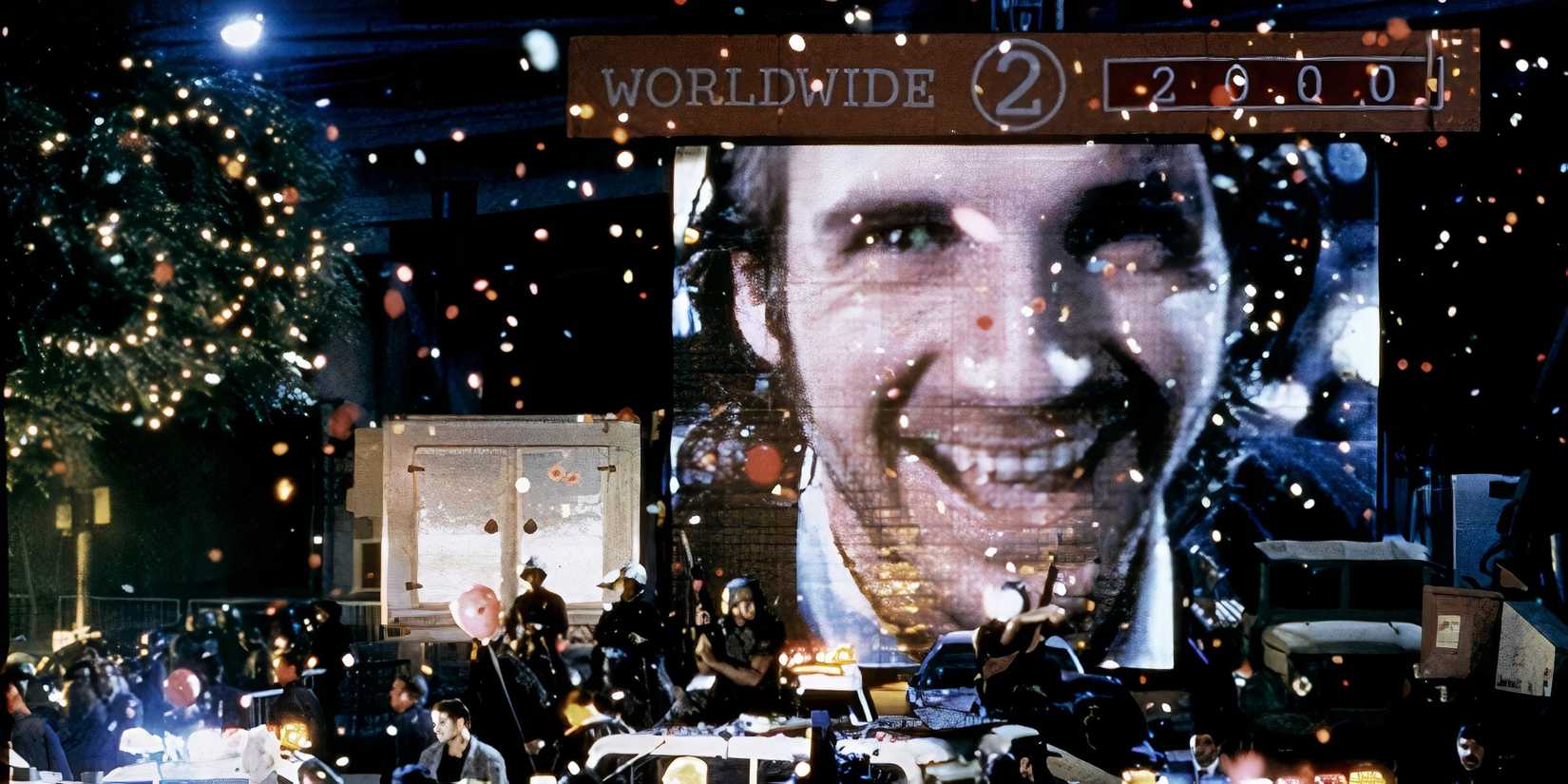 Ralph Fiennes smiles on a big sign over a street scene with people celebrating the New Years in Strange Days