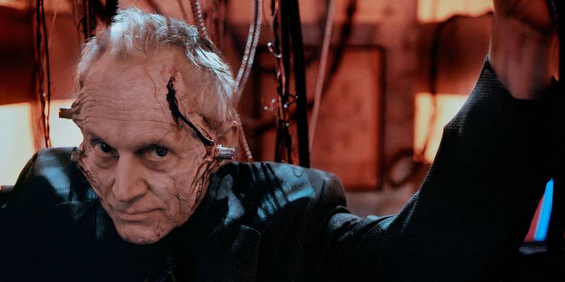 Lance Henriksen smirks withe metal tubes coming out of his face in The Mangler 2