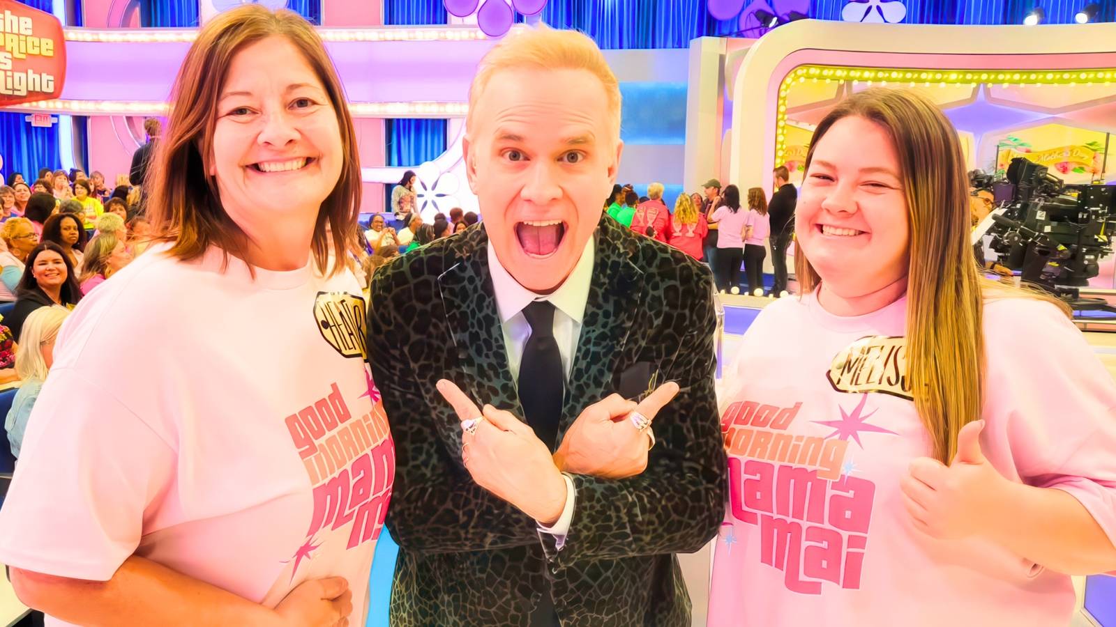 The Price Is Right's George Gray smiles while pointing at two studio audience members