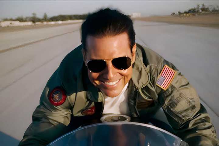 Tom Cruise smiling while riding a motorcycle in Top Gun Maverick
