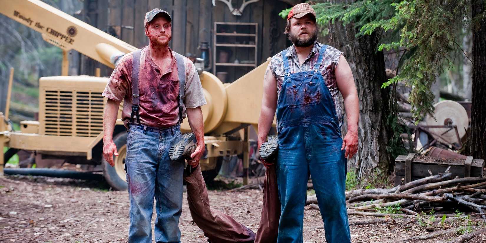 Tucker e Dale em roupas ensopadas de sangue enquanto seguram as pernas de um cadáver em Tucker & Dale vs Evil