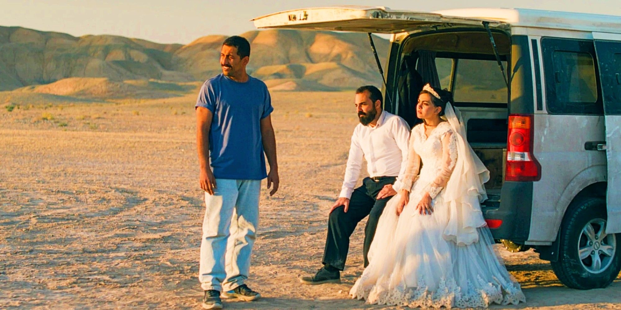 Два мужчины и женщина в свадебном платье сидят рядом с фургоном в пустыне в фильме "It Was Just An Accident"