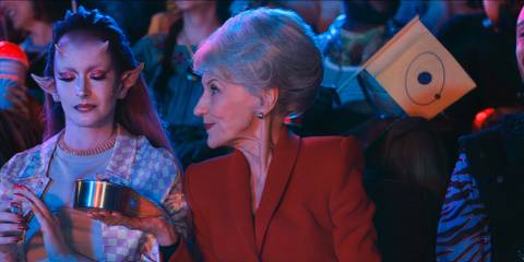 Mrs. Flood holding up a tin to an alien in a crowded theater