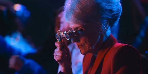 Anita Dobson as Mrs. Flood looking through opera glasses
