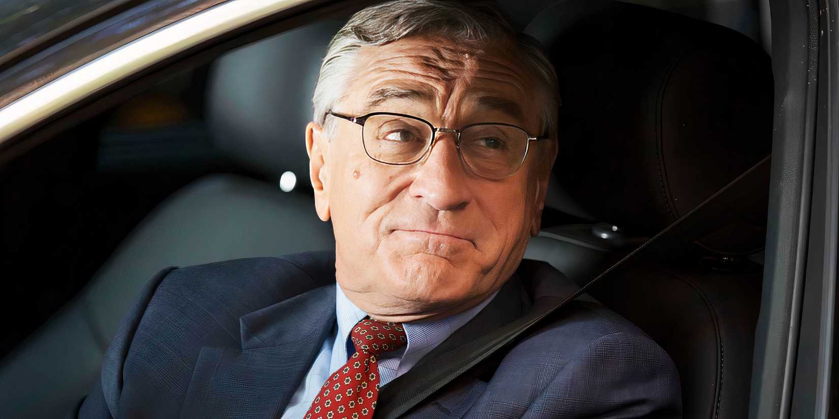 Ben looks up while smiling behind the wheel of a car in The Intern