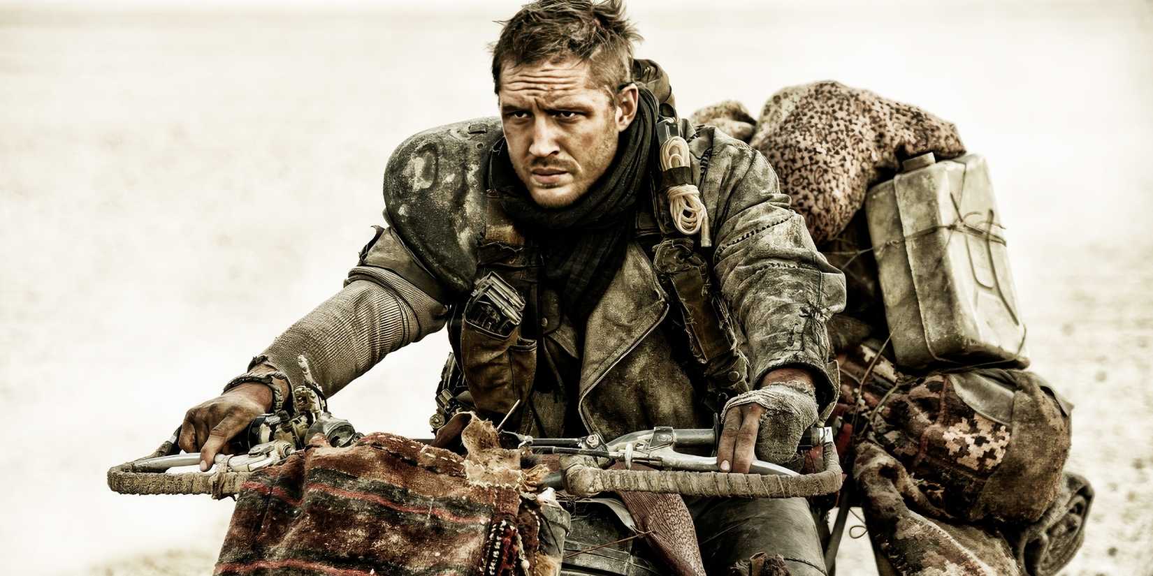 Tom Hardy as Max riding a bike and looking grumpy in Mad Max: Fury Road