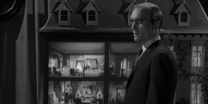 Charley (Robert Duvall) parado ao lado de uma casa de boneca na miniatura da zona de Twilight.