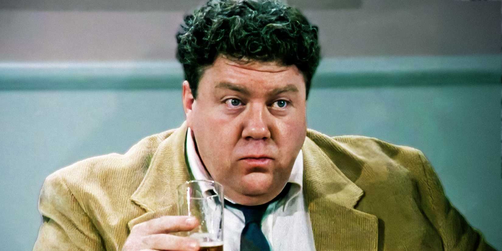 George Wendt como Norm Peterson segurando um copo de cerveja em Cheers