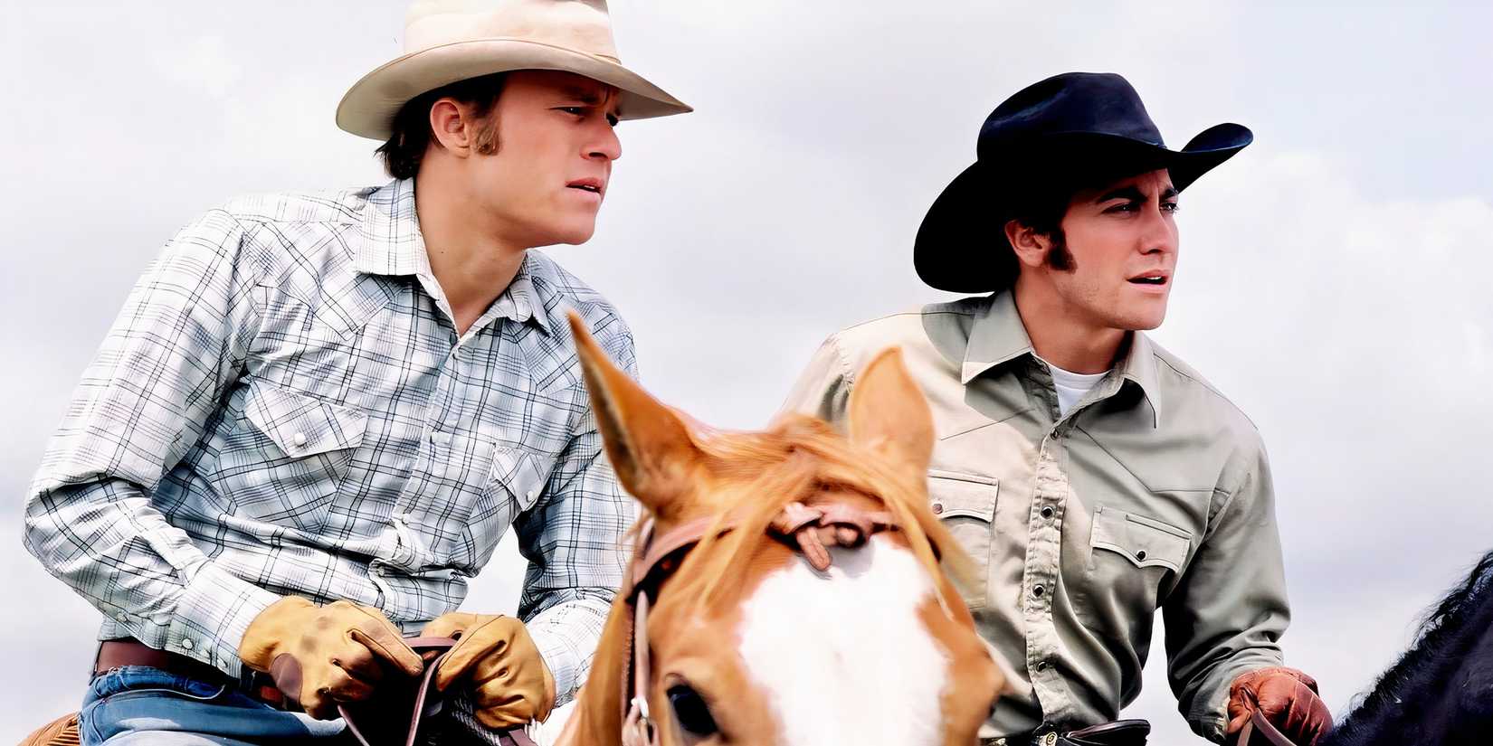 Heath Ledger and Jake Gyllenhaal ride horses next to each other and squint off into the distance in Brokeback Mountain
