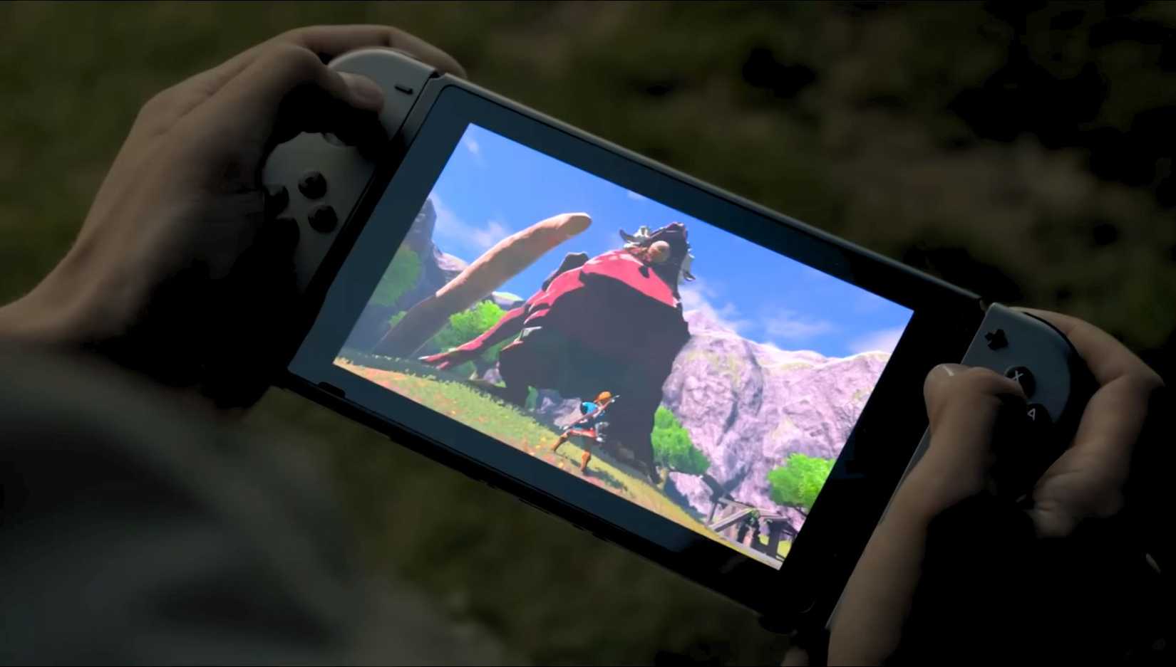 Hands holding an original Nintendo Switch that's showing Link in Zelda_ Breath of the Wild on screen