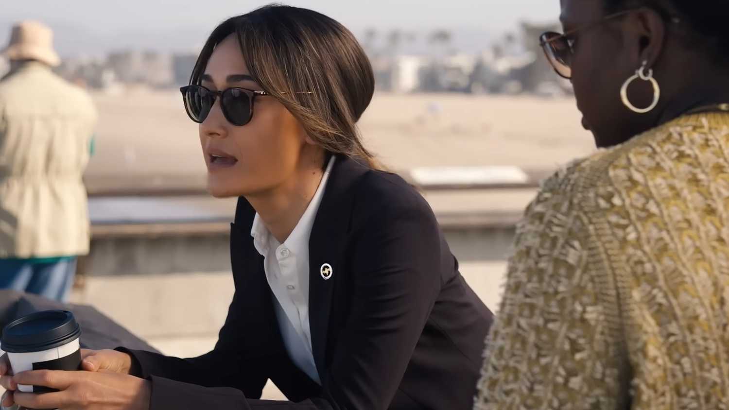 Maggie Q's Renée holding a coffee cop and leaning over a railing while talking to Courtney Taylor's Samira Parker in Ballard