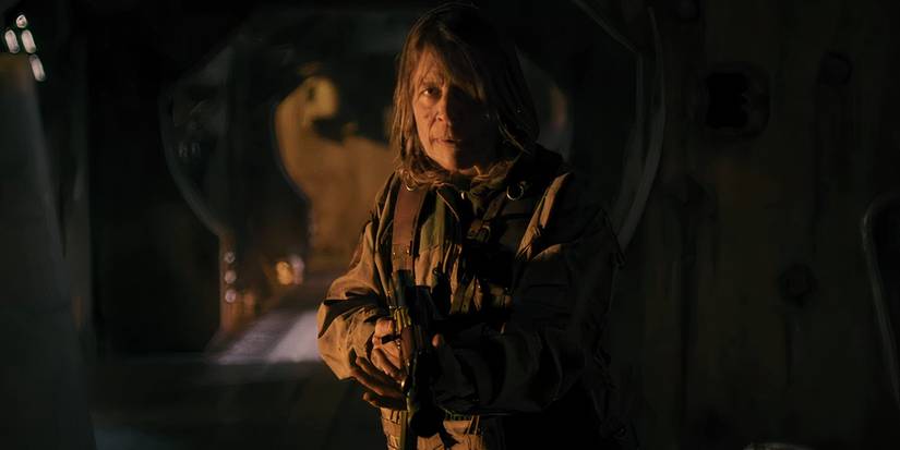 Linda Hamilton como Anya olhando intensamente por um corredor com seu rifle em Osiris