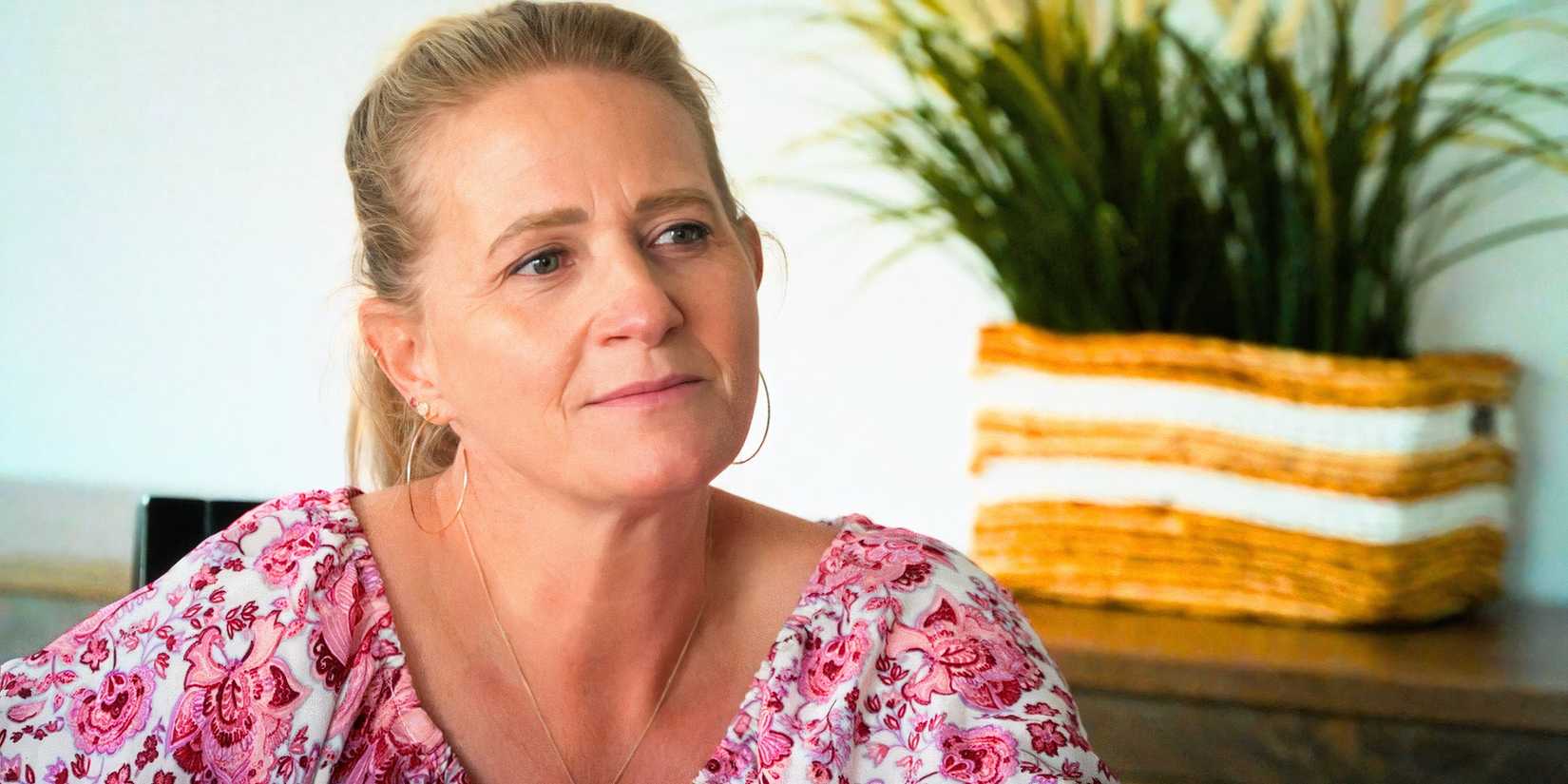 sister wives star christine brown smilng in a pink bouse with a houseplant in the background