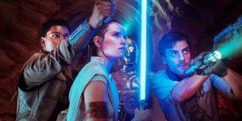 Poe Dameron and Finn holding up blasters on either side of Rey who is holding a blue lightsaber in The Rise of Skywalker