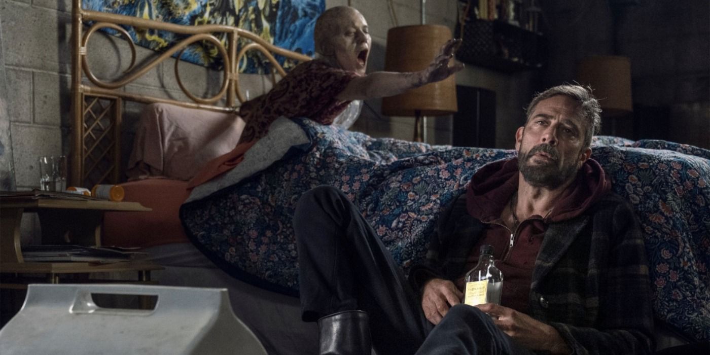 Negan sits on the floor with a bottle of booze with the zombiefied Lucille in the bed behind him