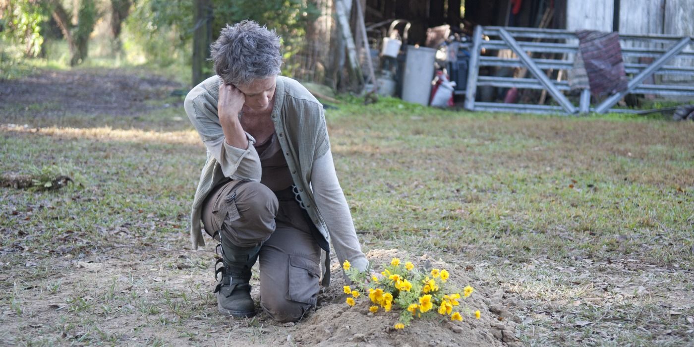 Carol looks down on yellow flowers on a grave in The Walking Dead
