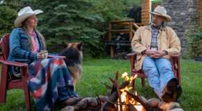 A woman sitting by an outdoor fire with a man and a dog in Heartland