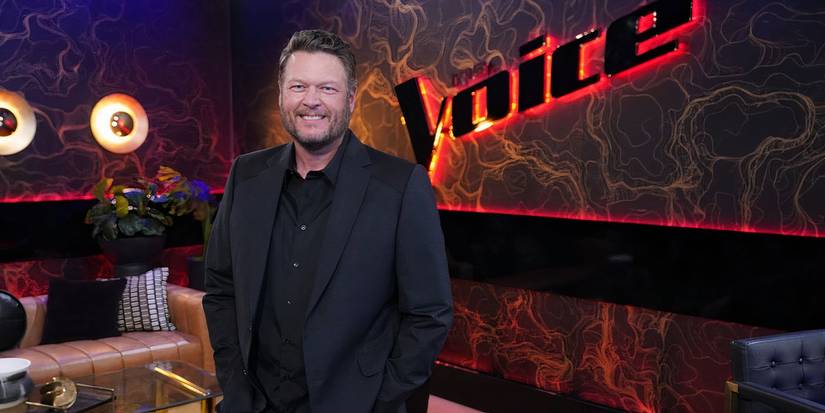 The Voice's Blake Shelton standing before show's logo