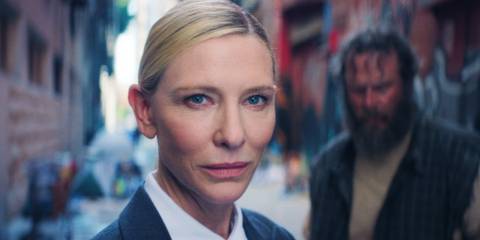 Cate Blanchett as the Recruiter smirking towards the camera while a bearded man stands behind her in Squid Game Season 3 Episode 6