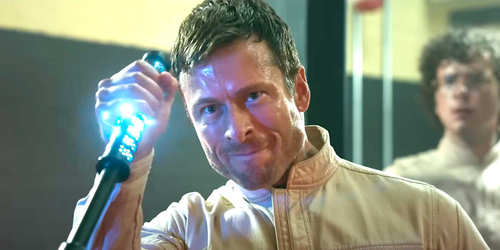 Glen Powell grips an electric prod and grimaces from The Running Man trailer