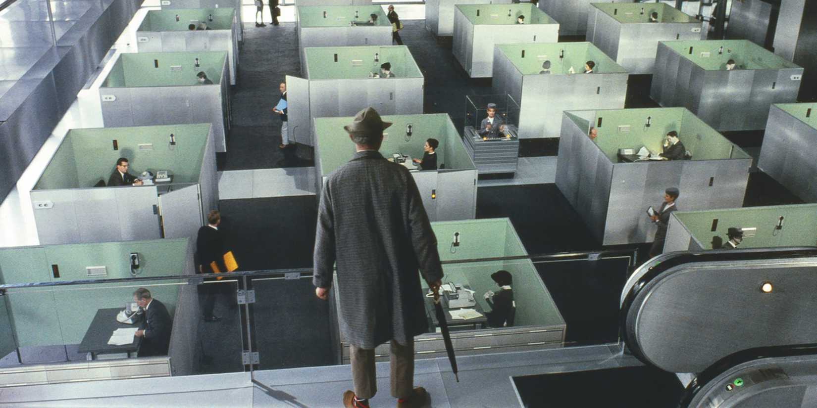 Mr. Hulot looks out over a large office filled with glᴀss cubicles in Playtime