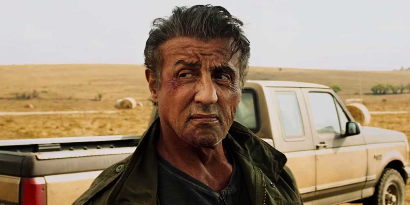 Rambo looks over his shoulder with a scowl in front of his truck in Rambo: Last Blood